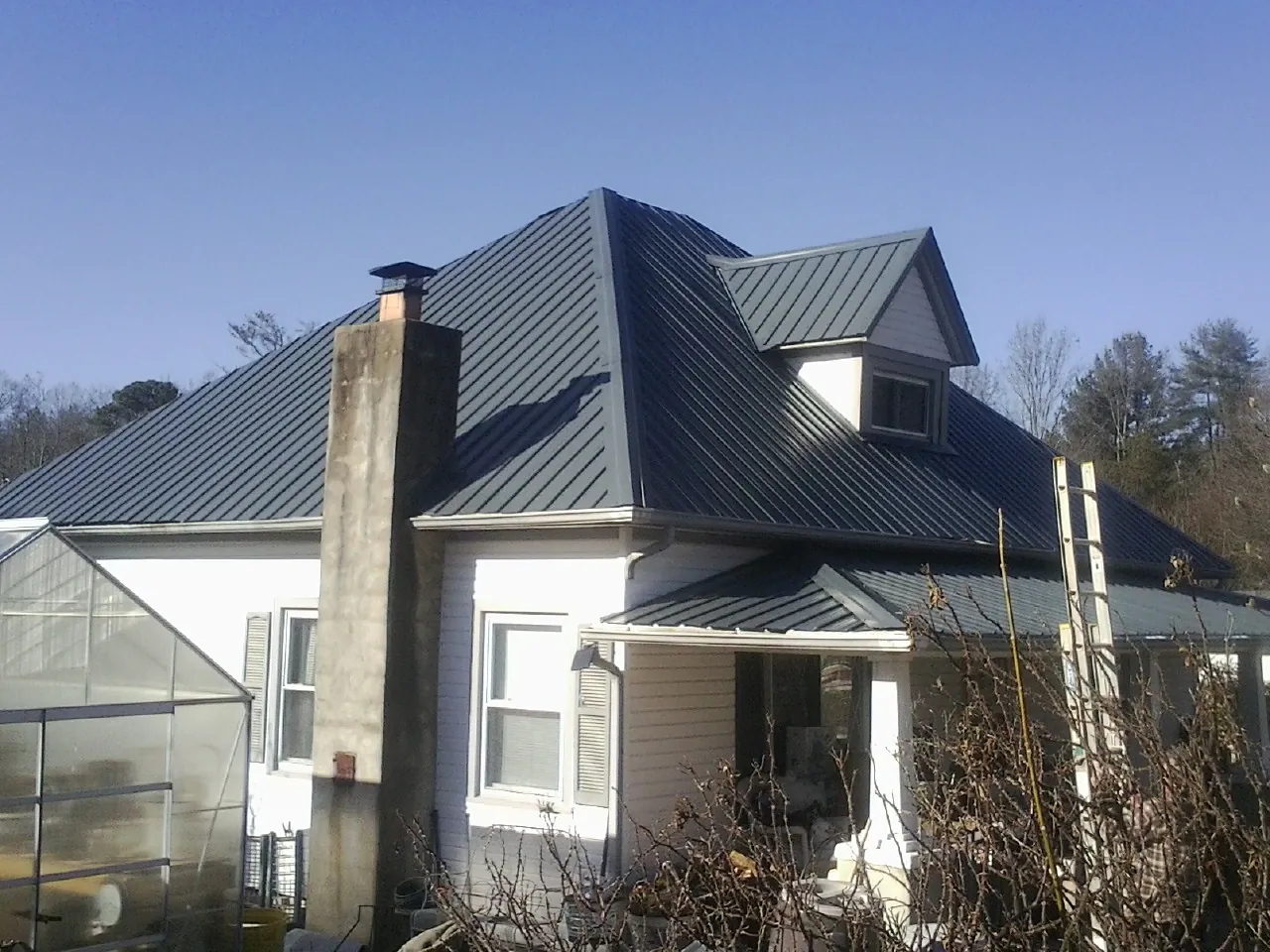 Dark blue standing seam metal roof on a white farmhouse with dormer — Slate & Tile Roof Repair by Roofing Brothers in Lawsonville
