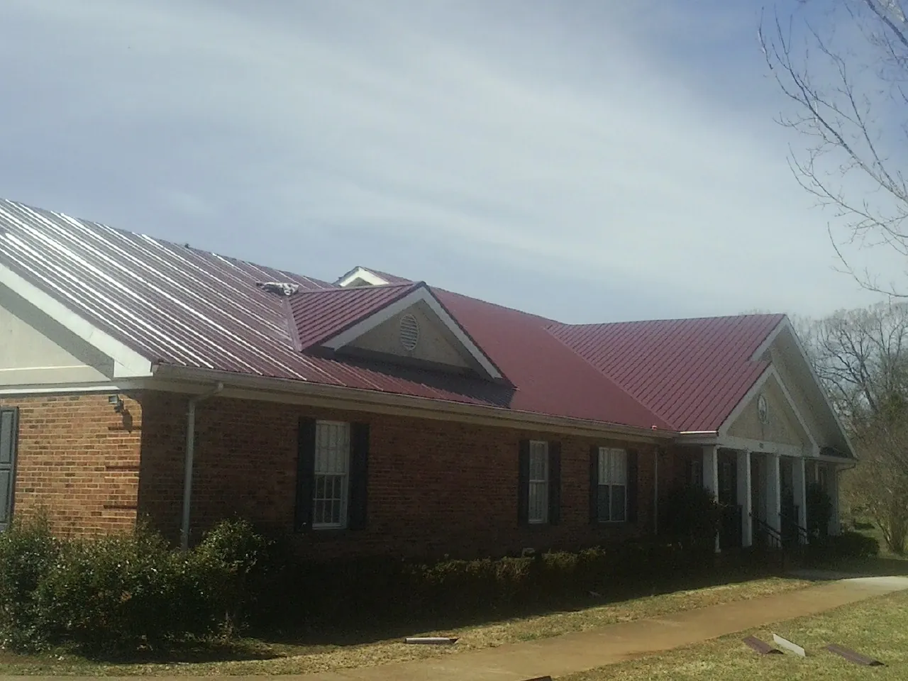 Red metal roof with gabled entries on a long brick building, from a Hail Damage Roof Repair job in Lawsonville