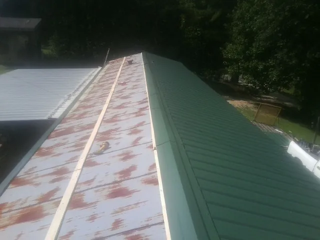 Old rusted panels beside newly installed green metal roofing — Wind Damage Roof Repair by Roofing Brothers in Lawsonville