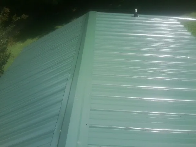 New green metal panels meeting at the ridge of a roof — Flat Roof Repair work by our crew in Lawsonville