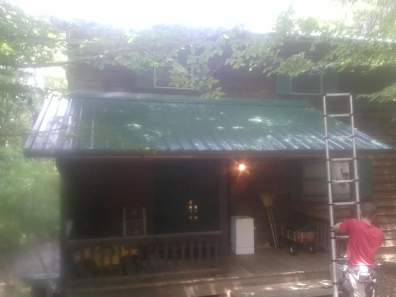 Worker on a ladder at the green porch roof of a wooded cabin in Lawsonville