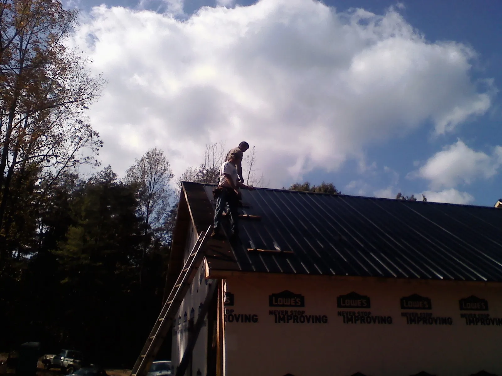 Roofer fastening dark metal panels high against a cloudy sky, from a Roof Inspection job in Lawsonville