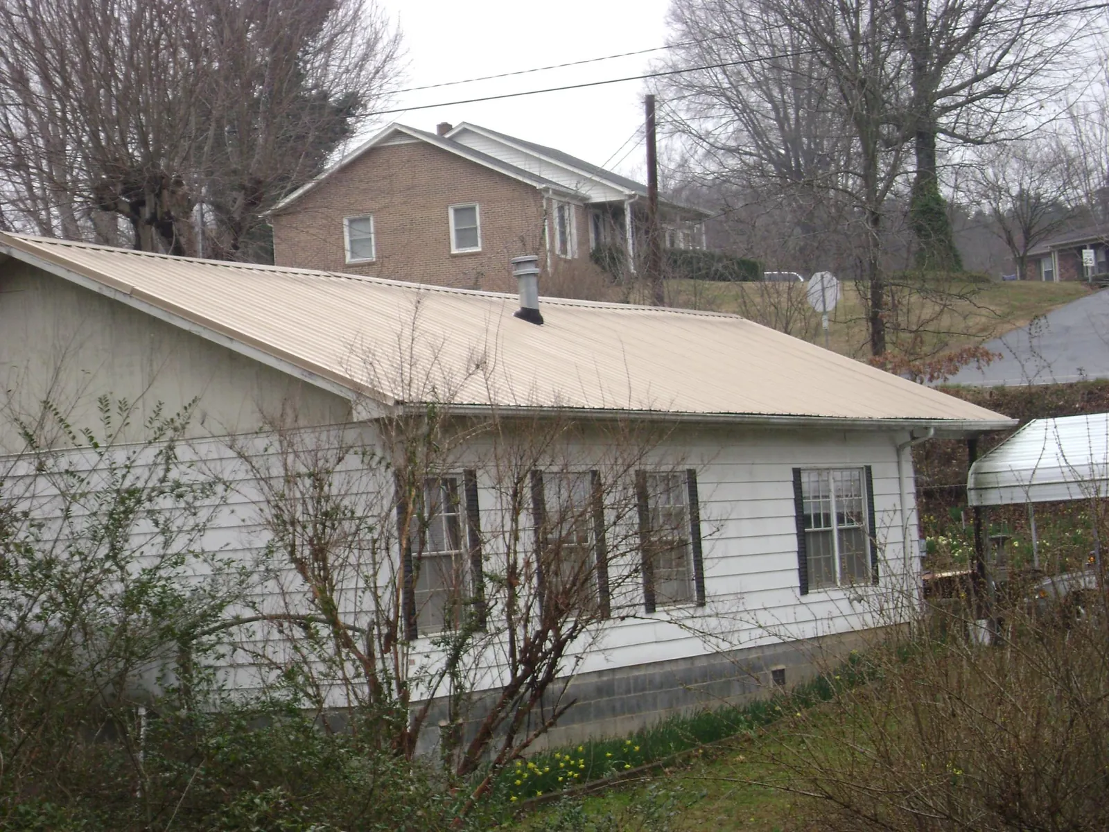 Tan metal roof on a white sided house set into a hillside — Commercial Roofing by Roofing Brothers in Lawsonville