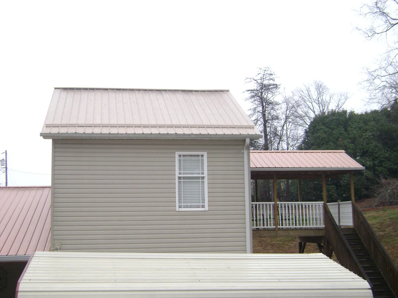 Tan metal roofs on a two story addition and attached porch, from a Roof Replacement job in Lawsonville